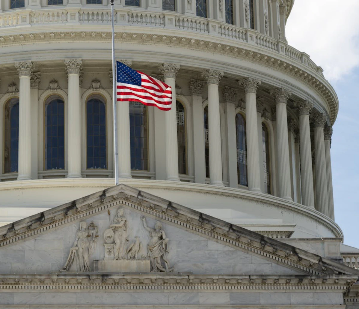 Close-up of the U.S. Capitol’s classical façade showing Corinthian columns, a sculpted pediment, and an American flag flying.